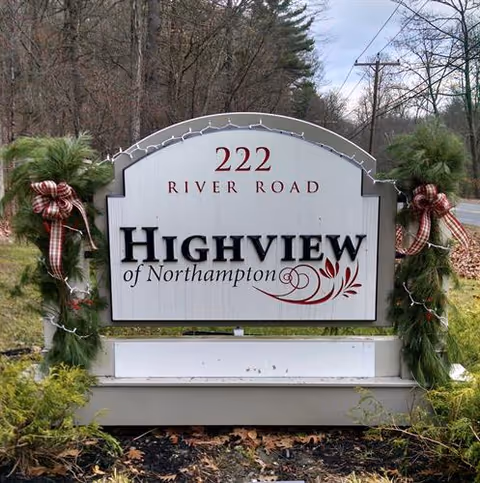 Outdoor sign for Highview of Northampton located at 222 River Road, decorated with green garlands and red plaid bows on either side.