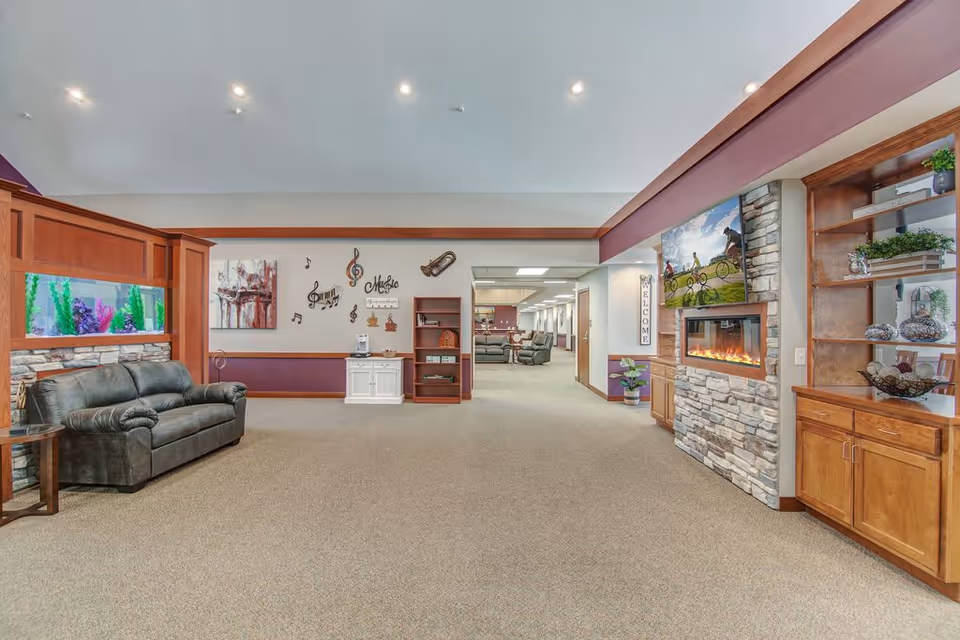 Spacious senior living lounge with sofas, an aquarium, a stone fireplace, and built-in shelving.