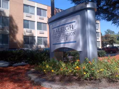 Exterior view of Raleigh Rehabilitation Center sign, brick building, and landscaped garden beds.