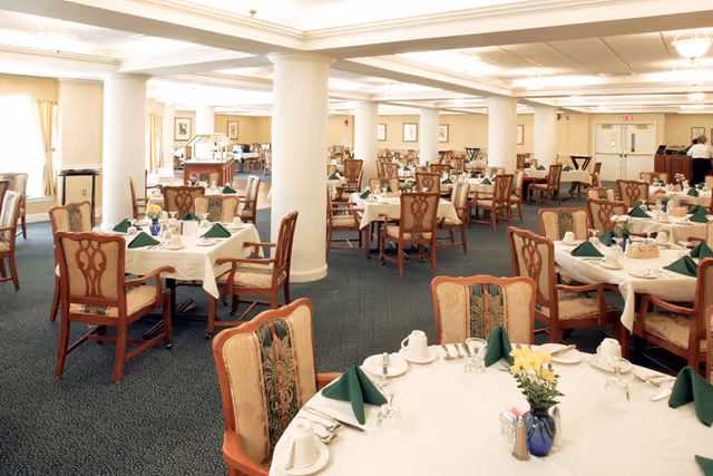 Large formal dining room with round tables set with white tablecloths, green napkins, and wooden chairs.