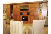 A cozy living room area with several upholstered chairs arranged facing a large wooden entertainment center that houses a flat-screen TV and a fireplace.