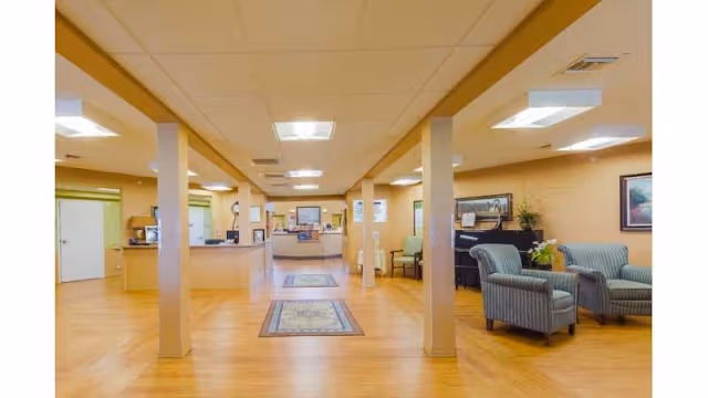 Spacious senior living facility lobby with a reception desk, seating area, columns, and hardwood floors.