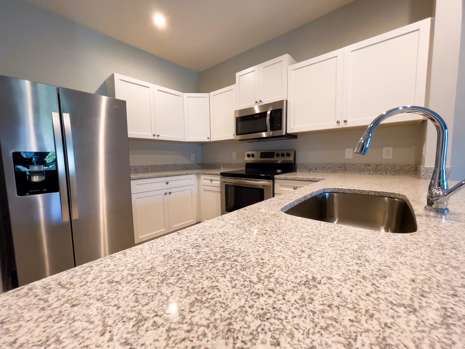Modern kitchen with white cabinets, granite countertops, stainless steel refrigerator, stove, microwave, and a sink with a curved faucet.