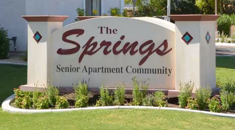 A large sign reading The Springs Senior Apartment Community sits in a landscaped lawn.