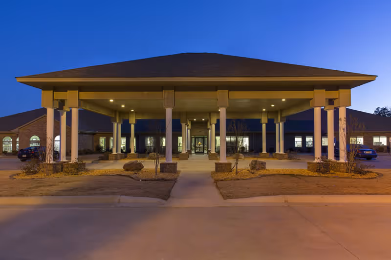 Covered porte-cochère entrance of a nursing and rehab facility illuminated at dusk.