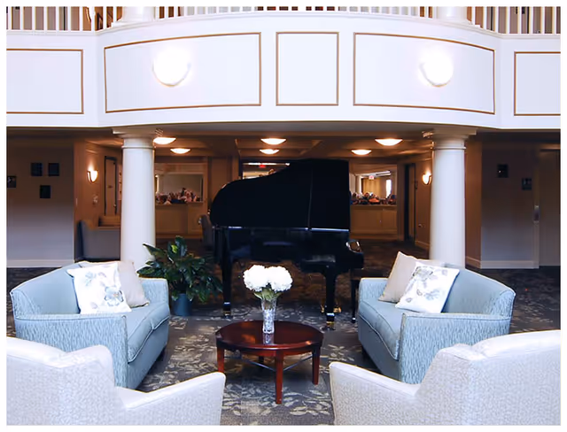 Cozy lounge with four upholstered chairs around a coffee table and a grand piano beneath an interior balcony.