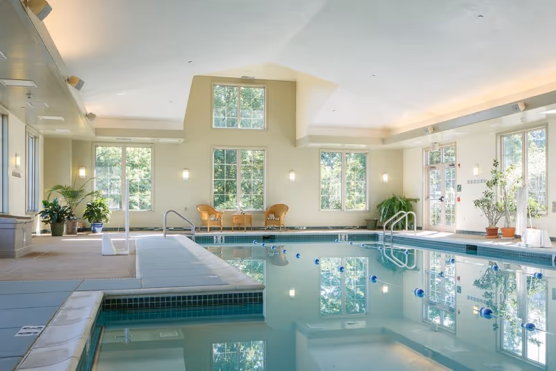 Indoor swimming pool and seating area at Southampton Estates with large windows, plants, and reflected ceiling lights.