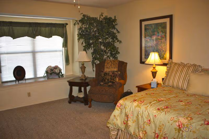 Cozy bedroom at Heatheridge Assisted Living with floral bedspread, armchair, and lamps.