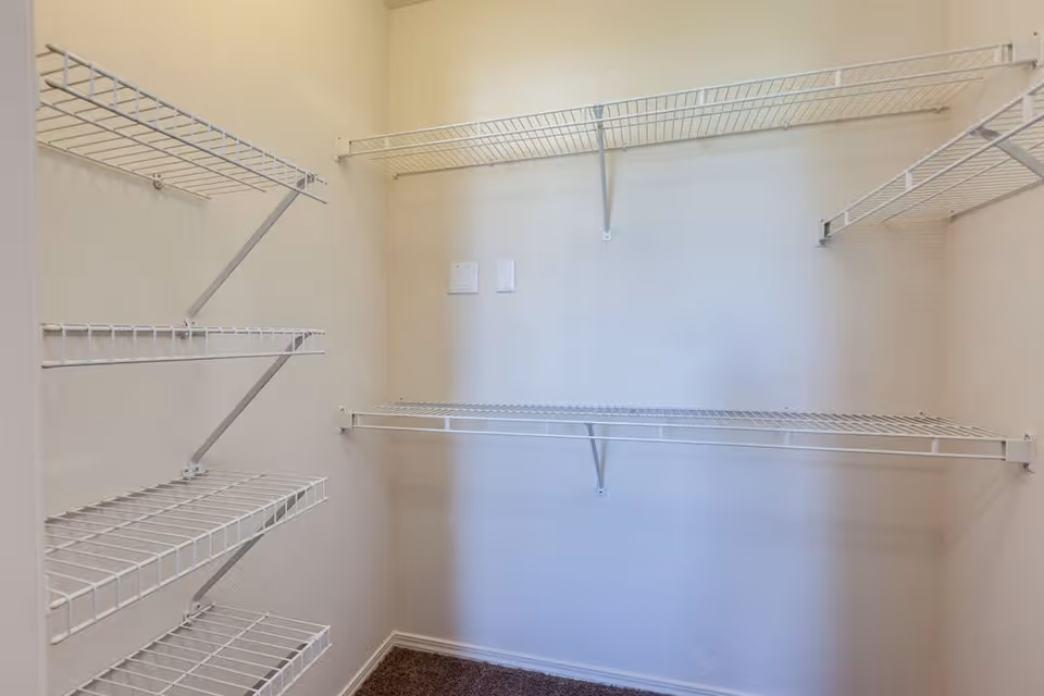Empty walk-in closet with white wire shelving on three walls and beige carpeted floor.