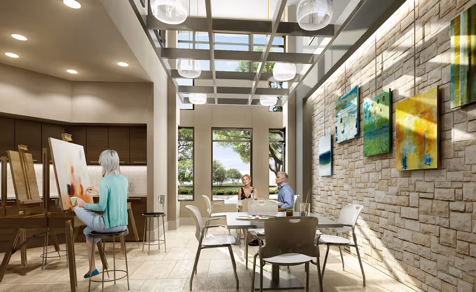 Bright communal activity room with seniors painting and chatting around tables beneath skylights and colorful wall art.