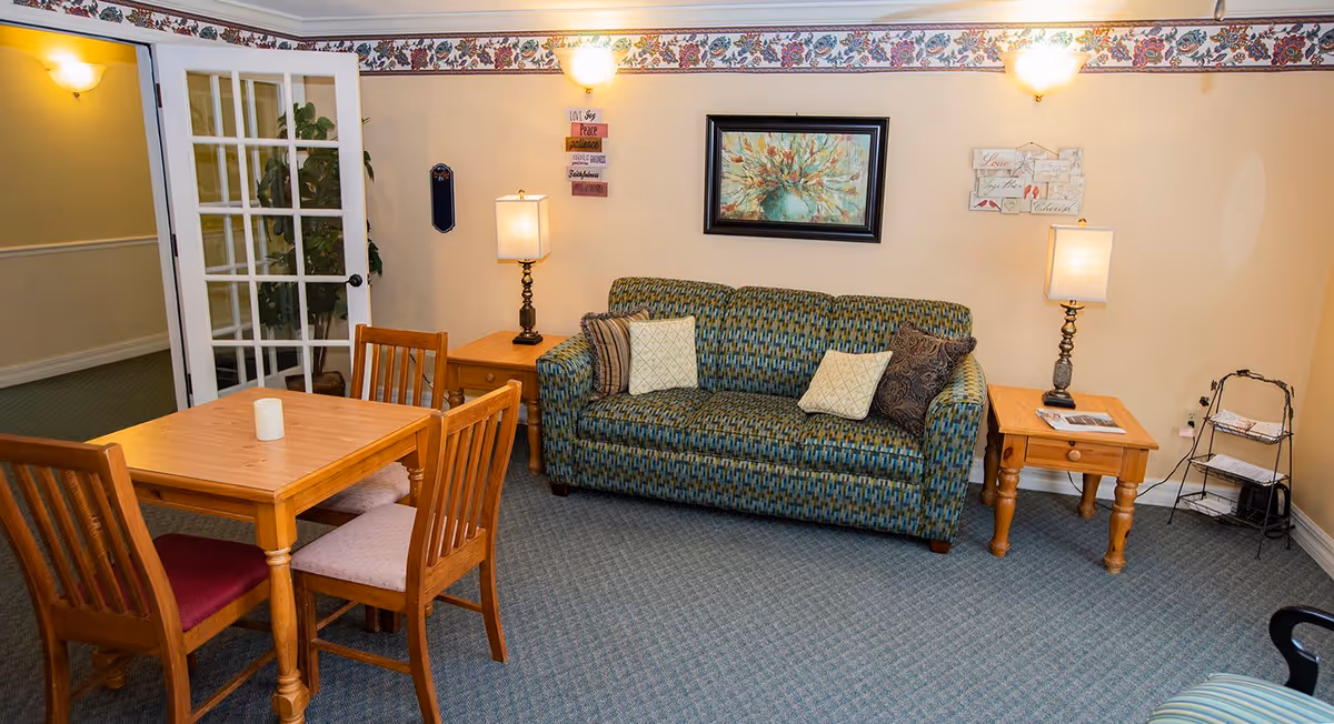 Cozy sitting area with a patterned sofa, side tables and lamps, and a wooden dining table with four chairs.