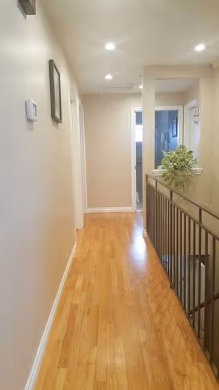 Bright hallway inside Sunset Home Care with hardwood floor, walls, framed art, and railing.
