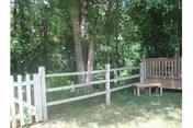 Small wooden split-rail fence and deck beside a grassy yard with dense trees in the background.
