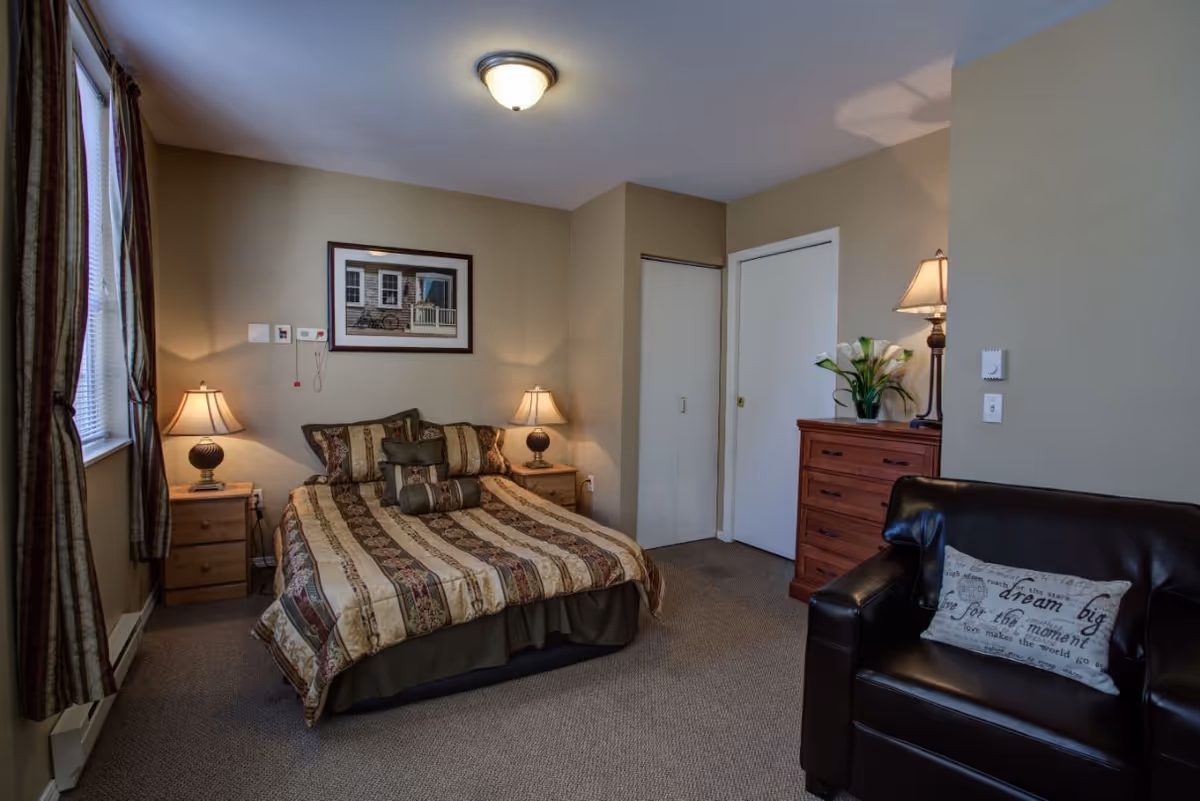 Furnished bedroom featuring a double bed with patterned bedding, bedside tables and lamps, a dresser, and a leather chair.