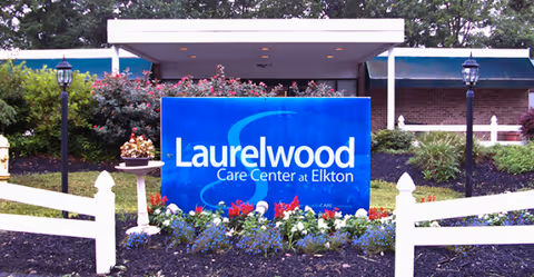 Front exterior of Laurelwood Care Center sign with colorful flowers and white fencing.