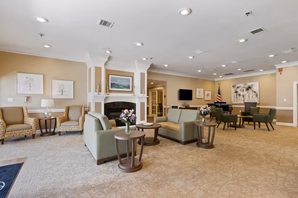 Spacious senior living common lounge with sofas, armchairs, side tables, a fireplace and artwork on the walls.