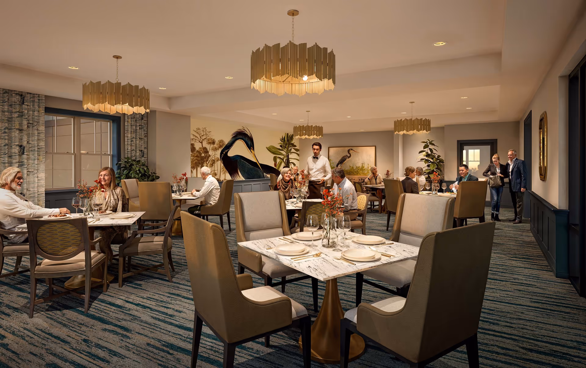 A well-lit dining room in a senior living facility with several tables set with plates, glasses, and floral centerpieces. Residents are seated at tables enjoying meals and conversation, while a waiter serves food. The room features modern chandeliers, large windows with curtains, and artwork of birds on the walls.