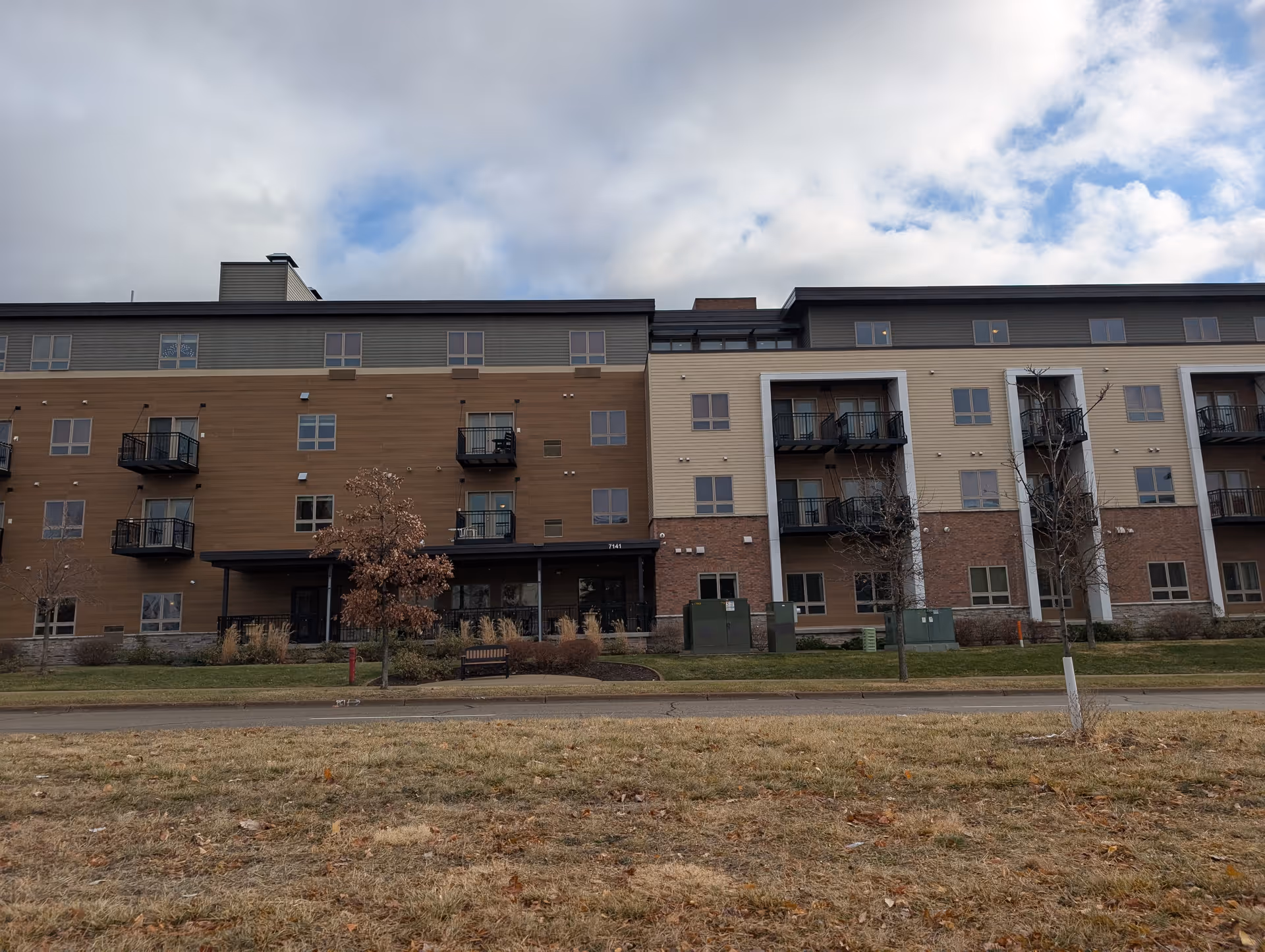 Four-story senior living building exterior with balconies, an entrance canopy, and a grassy foreground.