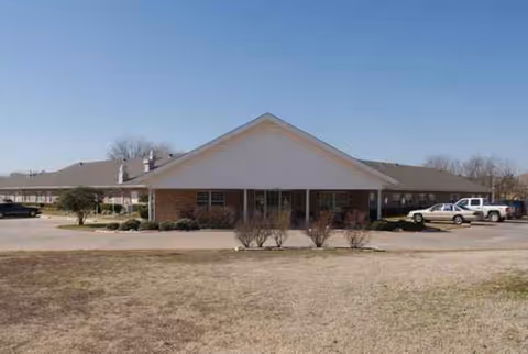 A single-story senior living facility front with a covered entrance and parked cars.