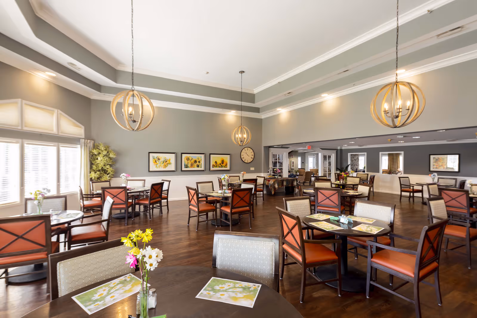 Bright, spacious dining room with round tables, chairs, floral centerpieces and decorative pendant lights.