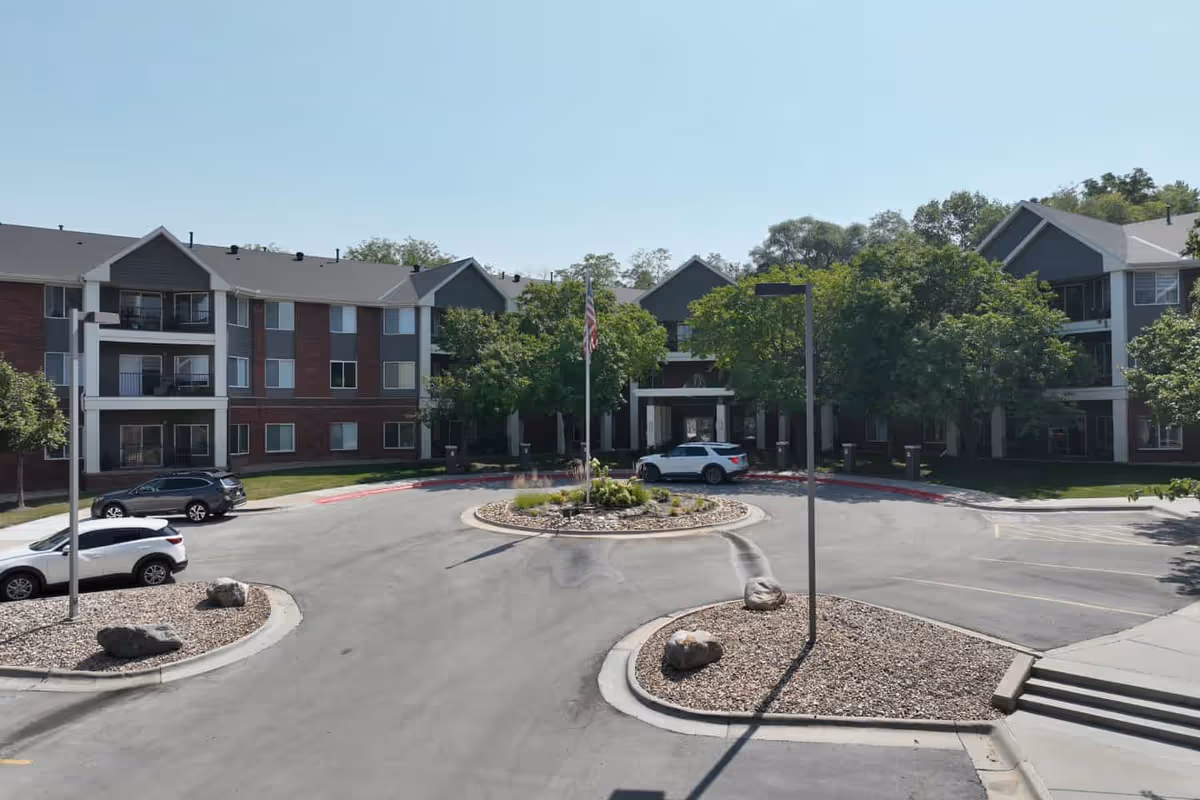 Exterior view of Arboretum Village senior living campus with brick and gray buildings around a circular driveway and landscaped center island.