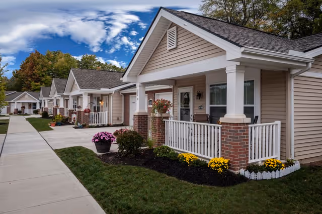 Row of single-story residential units with front porches, landscaped lawns, and a sidewalk.