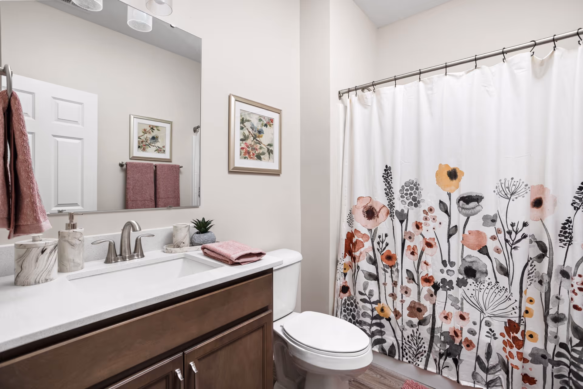 Bright bathroom featuring a vanity with sink and mirror, toilet, and a floral-patterned shower curtain.
