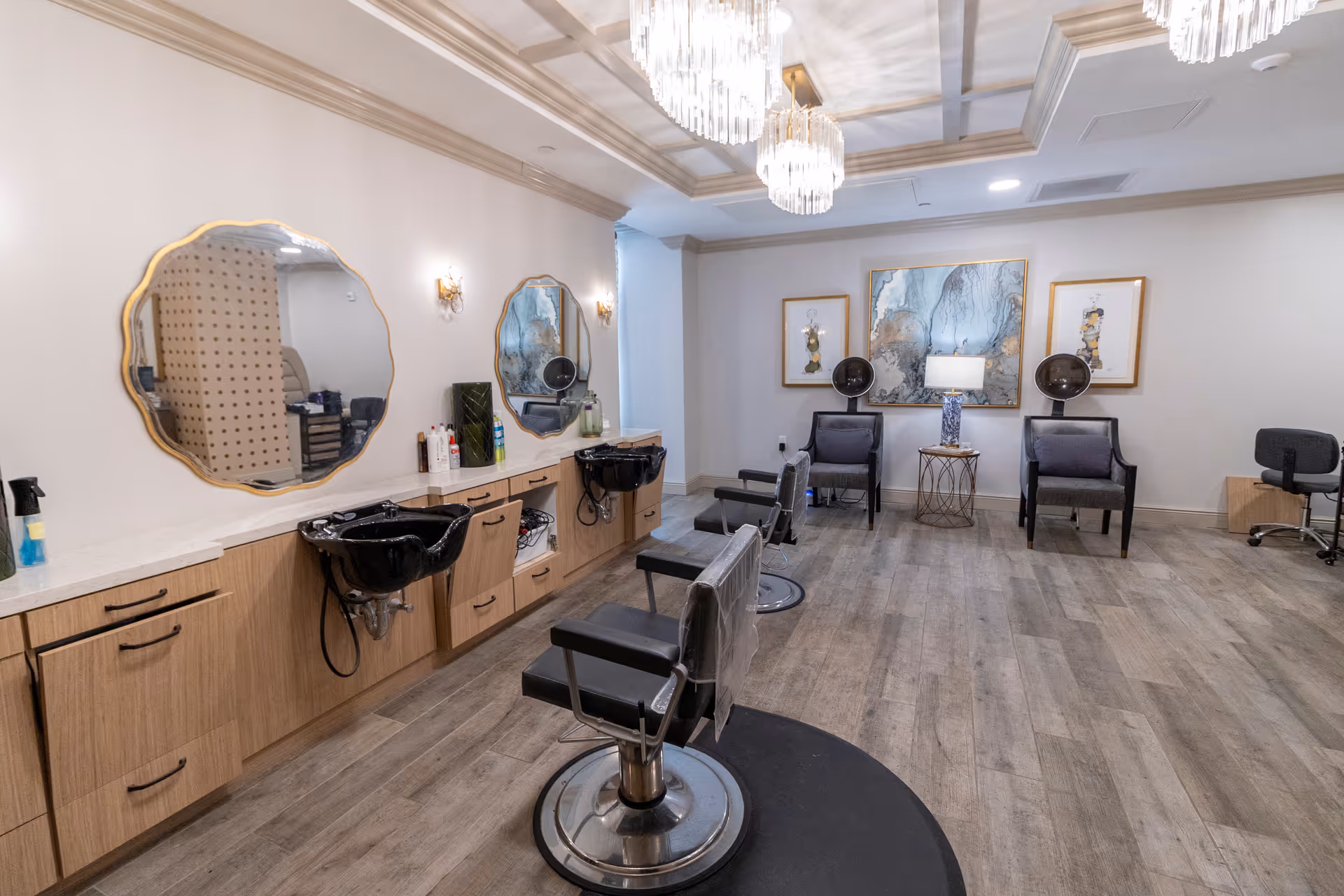 Salon-style interior with styling chairs, shampoo sinks beneath decorative mirrors, and waiting chairs under chandeliers.