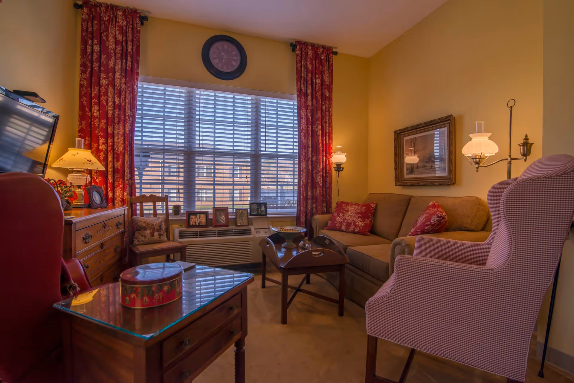 Cozy living room featuring a sofa and patterned armchairs, a coffee table and lamps in front of a large window with red curtains.