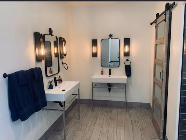 Two sink vanities with mirrors and wall lights in a clean, modern bathroom.