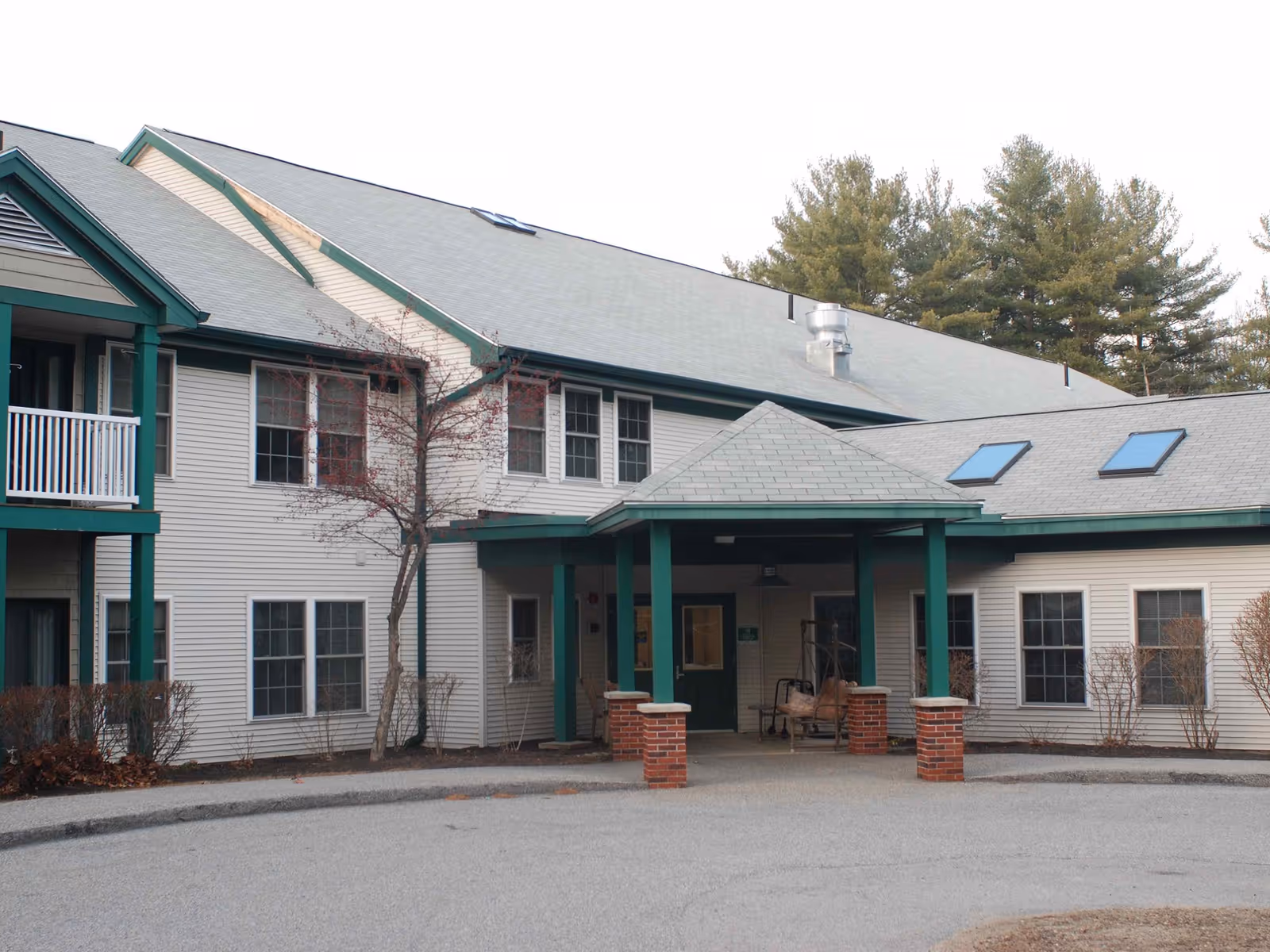 Front entrance of a two-story senior living building with a covered porte-cochere, green trim, and multiple windows.
