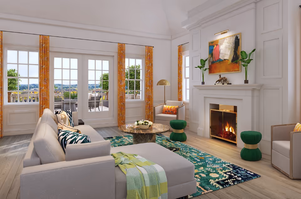 A bright and spacious living room with large windows and glass doors leading to an outdoor patio. The room features a light gray sectional sofa with patterned pillows, a round marble coffee table, two green cushioned stools, an armchair with a colorful pillow, a fireplace with a fire burning, and a colorful abstract painting above the mantel. The floor is wooden with a vibrant patterned rug, and orange curtains frame the windows.