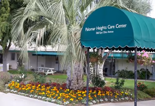 Exterior view of the Palomar Heights Care Center with a green awning and flowering garden.