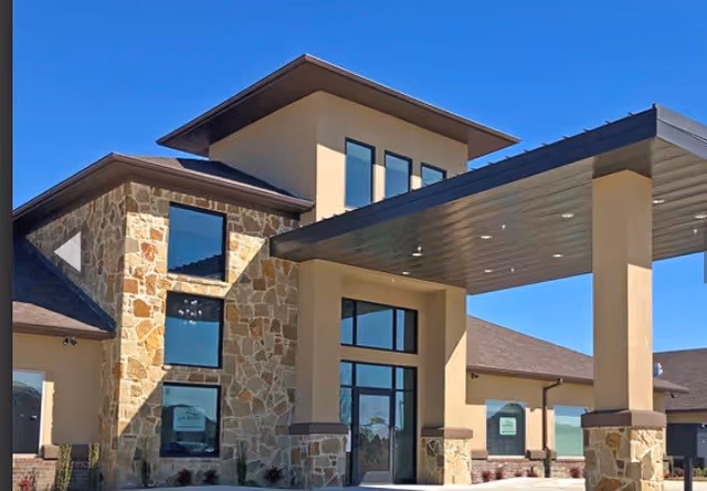 Entrance and porte-cochere of a modern stone-and-stucco senior living facility under a clear blue sky.