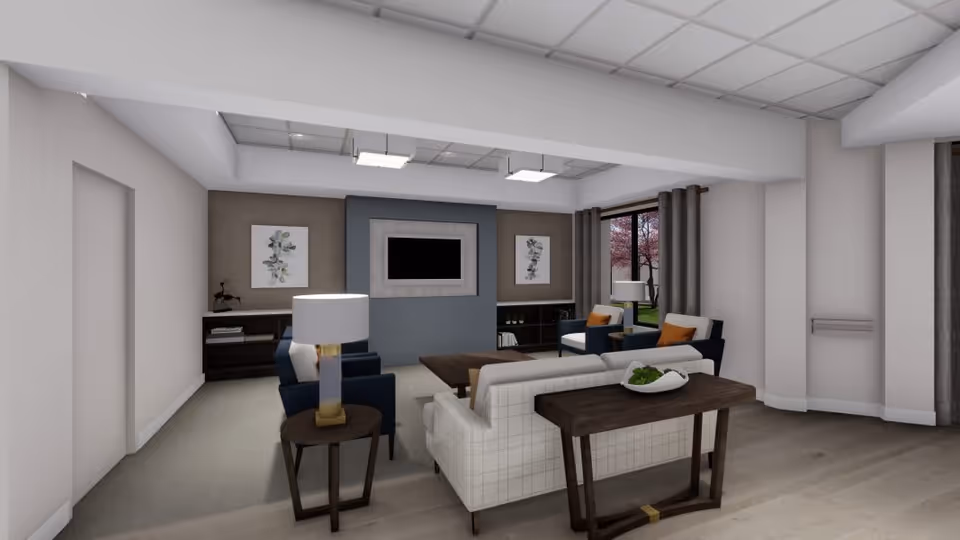 A modern living room in a senior living facility with a white couch, two blue armchairs with orange cushions, a wooden coffee table, and side tables with lamps. The room features a wall-mounted TV, two framed botanical prints, large windows with gray curtains, and a view of trees outside.