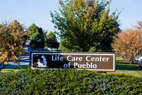 Outdoor sign for Life Care Center of Pueblo with trees and greenery around.