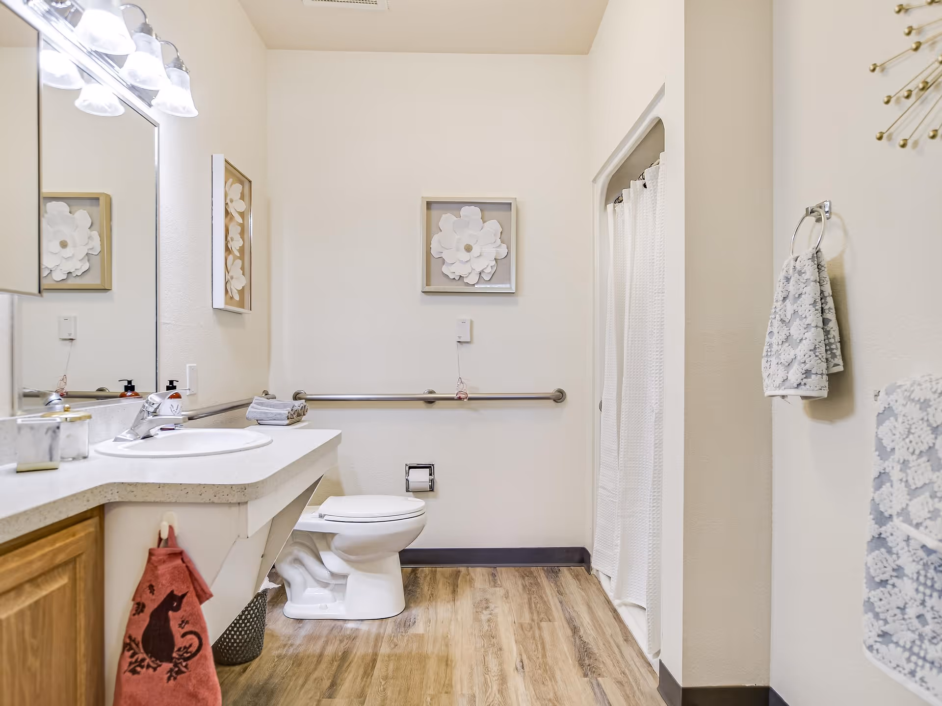 Well-lit accessible bathroom with a sink and mirror, toilet with a grab bar, and a shower with a white curtain.