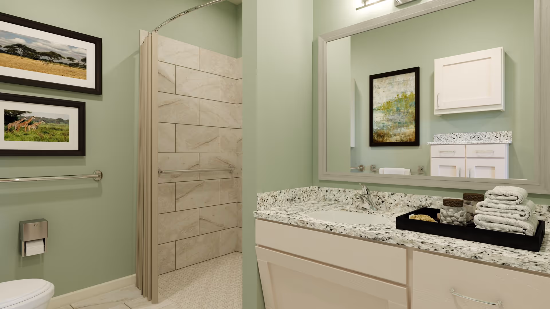 A bathroom with light green walls featuring a toilet with a mounted toilet paper holder, two framed pictures of nature scenes, a walk-in shower with beige tiles, and a vanity with a granite countertop. On the countertop, there is a black tray holding neatly folded white towels and decorative jars. A large mirror above the vanity reflects a white cabinet and a framed artwork.