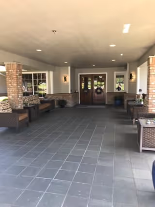 Covered entrance area with tiled floor, wicker seating with cushions on both sides, brick pillars, and double wooden doors at the far end with windows on either side.