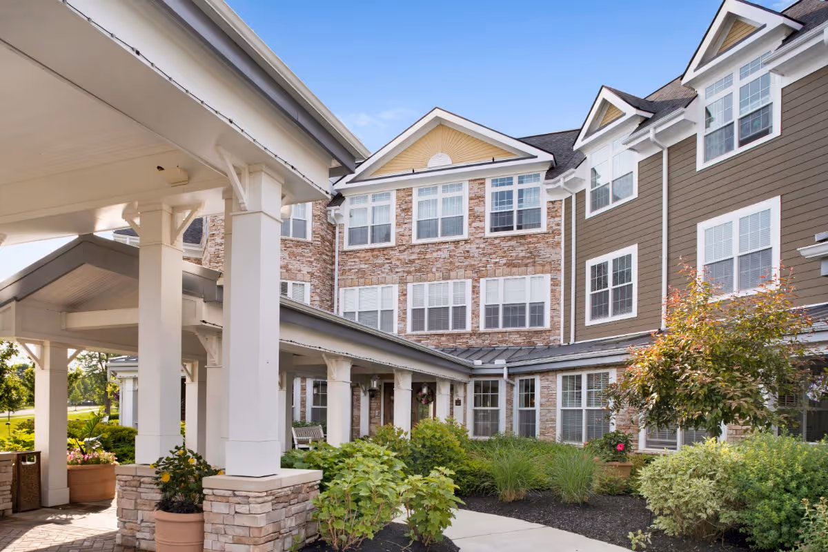 Covered entrance and landscaped front facade of a multi-story senior living building with brick and siding exterior.