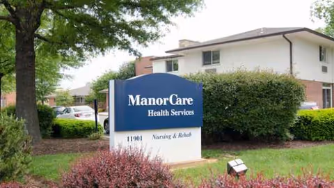 Exterior view of ManorCare Health Services sign near a building and greenery.