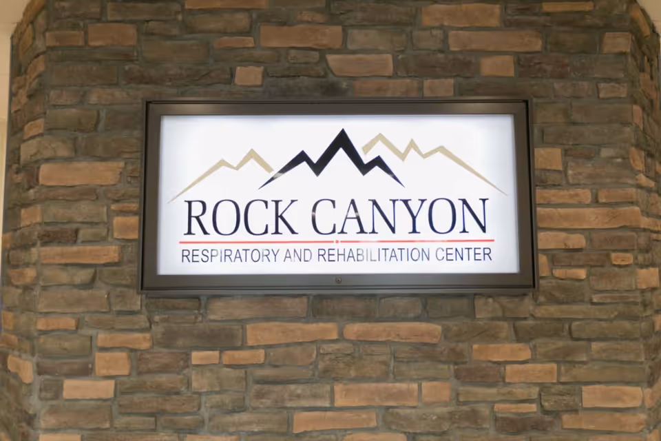 Illuminated Rock Canyon Respiratory and Rehabilitation Center sign mounted on a stone brick wall.