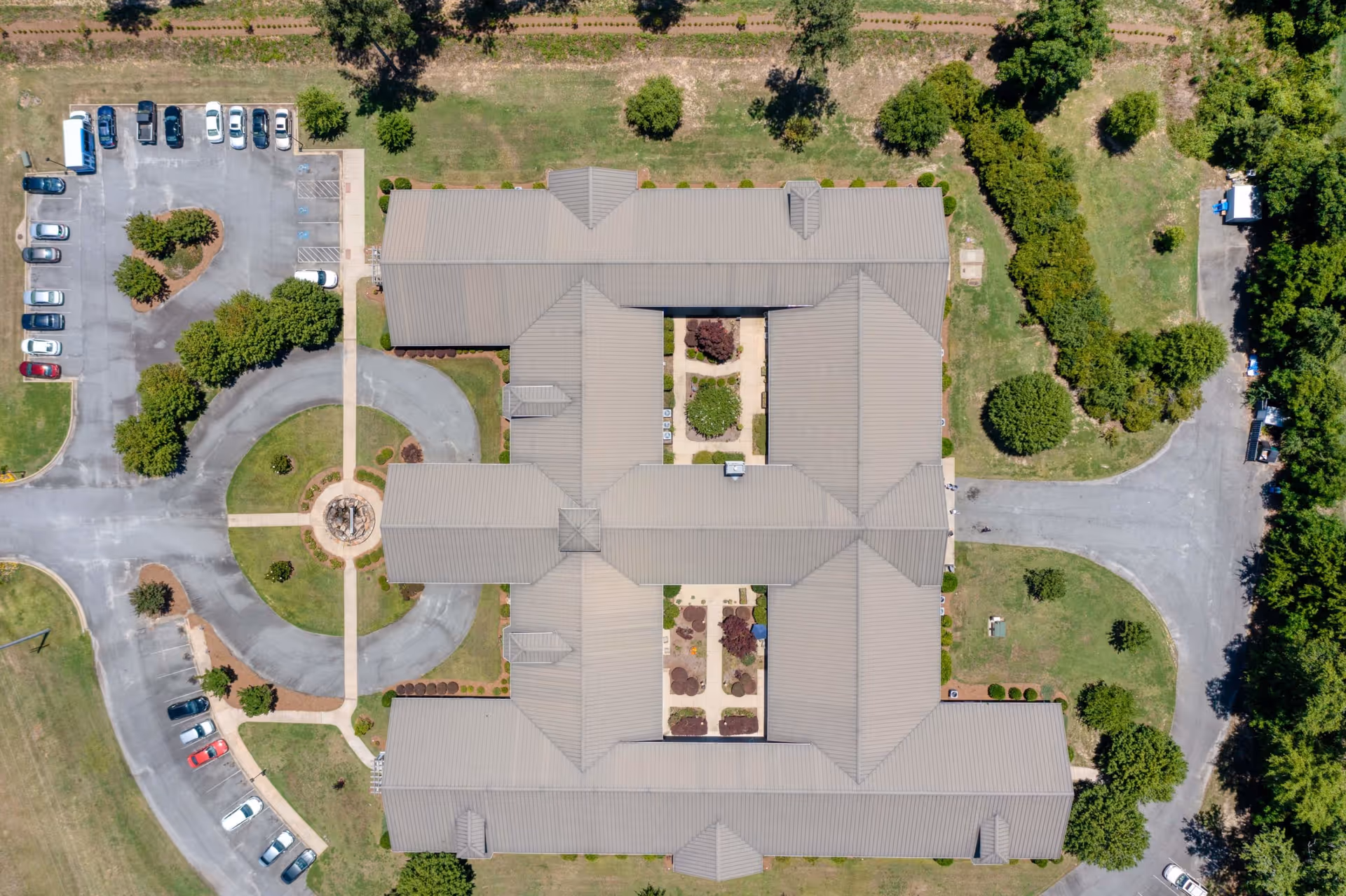 Aerial view of Addington Place of Dublin senior living facility showing the building's roof, surrounding parking lots with cars, circular driveway, landscaped gardens, and green grassy areas with trees.