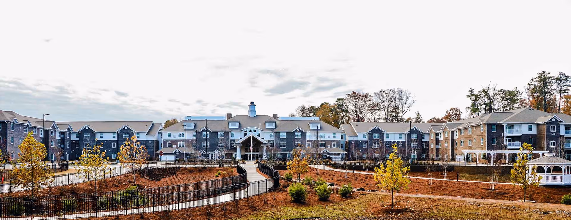 Panoramic exterior view of Vickery Rose Retirement Resort showing the multi-story building, landscaped grounds, walkways and gazebos.