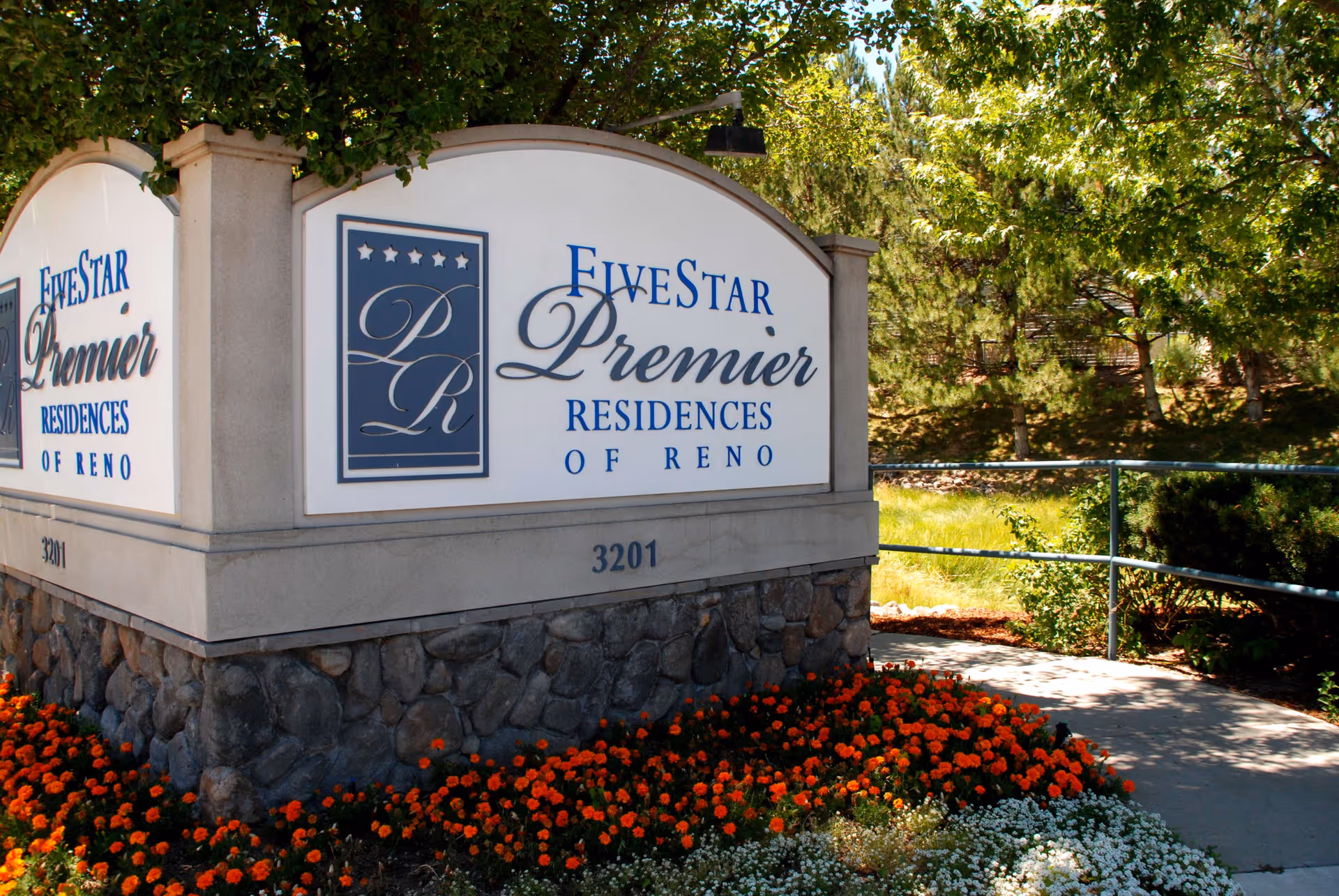 Stone-framed entrance sign reading "FiveStar Premier Residences of Reno" next to flower beds and a walkway.