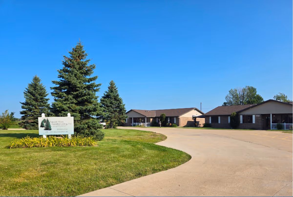Single-story brick senior living facility with curved driveway, manicured lawn, and a sign reading Patient Pines.