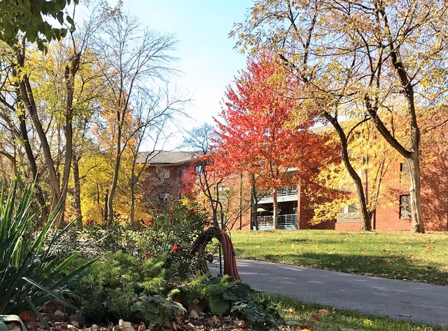Autumn trees and a brick senior living building along a paved walkway.