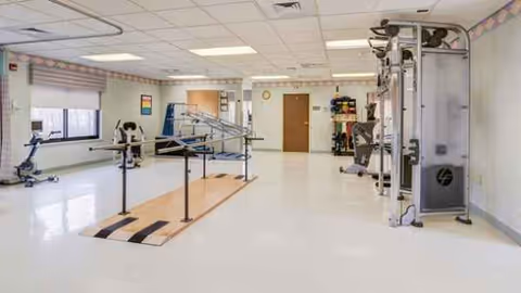 Indoor rehab gym at Legacy Hillsboro with parallel bars and exercise equipment.