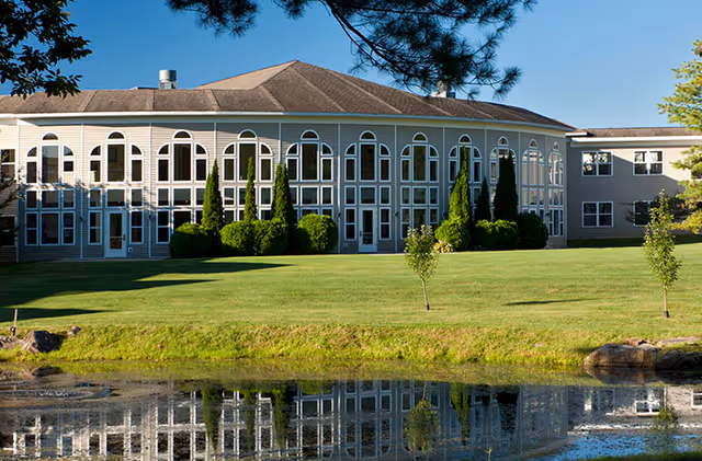 Prestwick Chase at Saratoga exterior building with arched windows, green lawn, and water reflection.