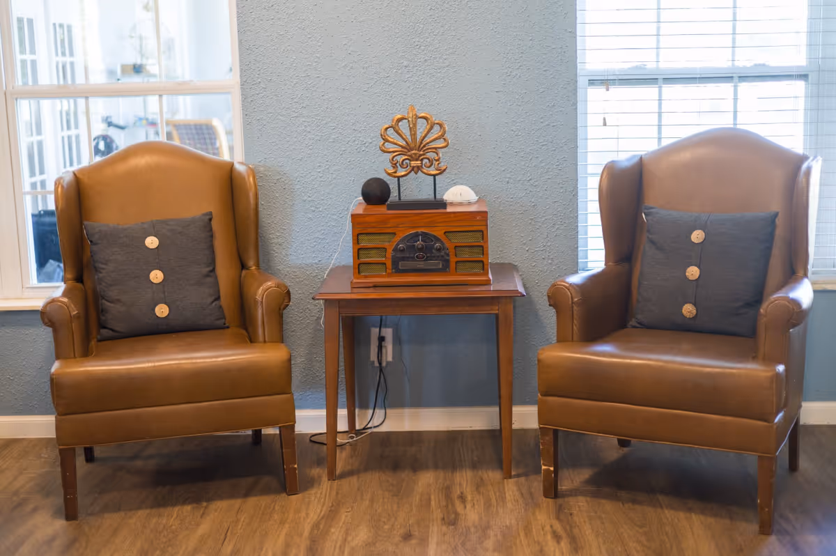 Two brown leather armchairs with blue buttoned pillows flank a small wooden table holding a decorative vintage radio against a blue wall.